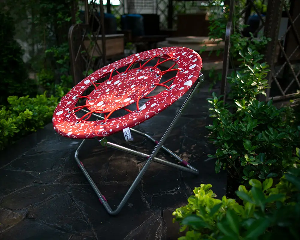 صندلی مدل بانجی قرمز رنگ با خالخالی های سفید در یک محیط سرسبز