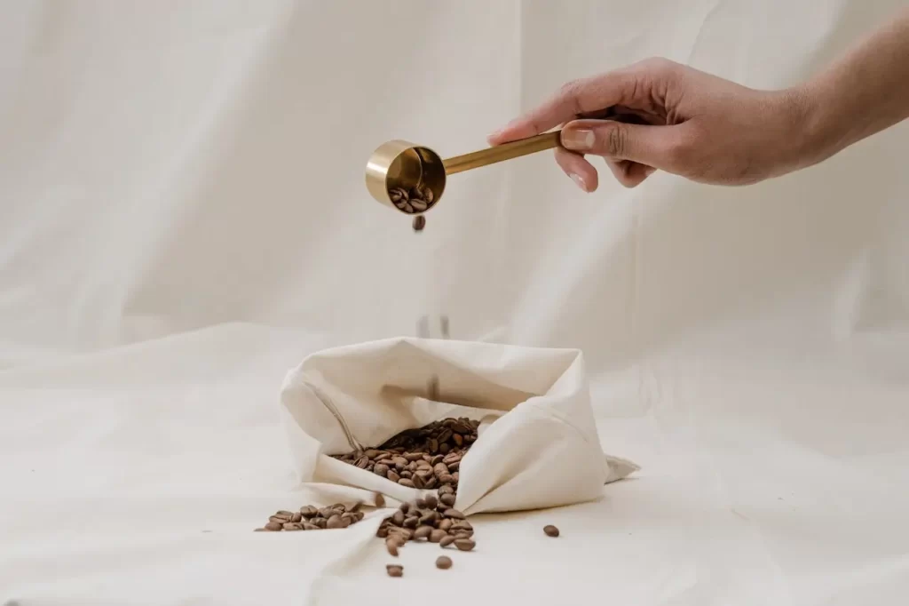 یک دست که با پیمانه دانه های قهوه را از داخل یک کیسه بیرون کشیده و دوباره به داخل کیسه میریزد
