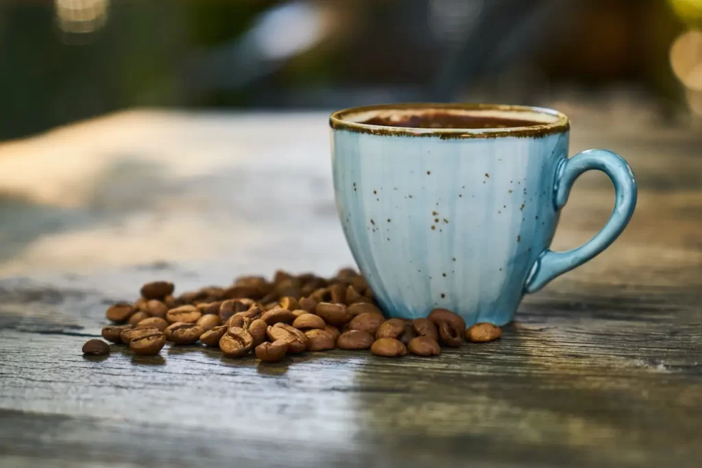 یک فنجان قهوه در کنار دانه های قهوه که کنا آن چیده شده اند